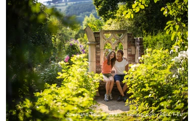 Mutter und Tochter sitzen in einem blühenden Garten und machen ein Selfie.