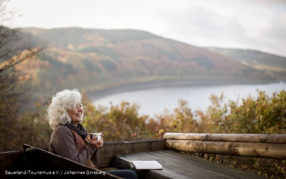 Eine Frau entspannt beim Lesen in der Herbstlandschaft um den Biggesee.
