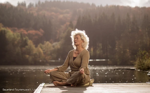 Ein Frau entspannt bei Yoga-Übungen an einem See.